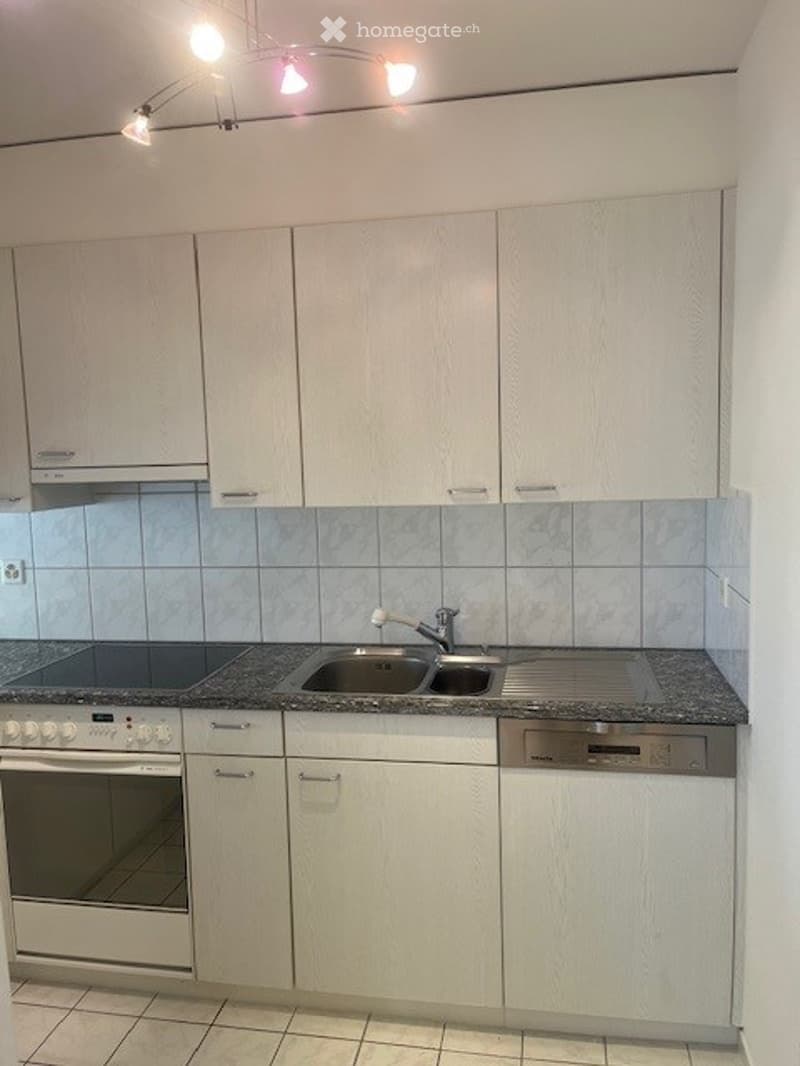 Modern kitchen with white cabinets, granite countertop, stainless steel sink, and built-in oven.