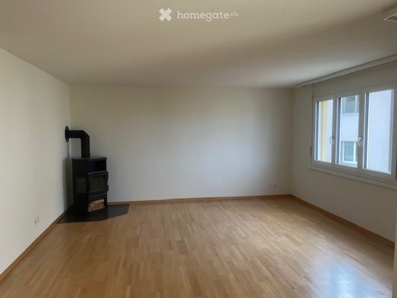 Empty room with wooden wall paneling, white walls, and a window with a view of another building.