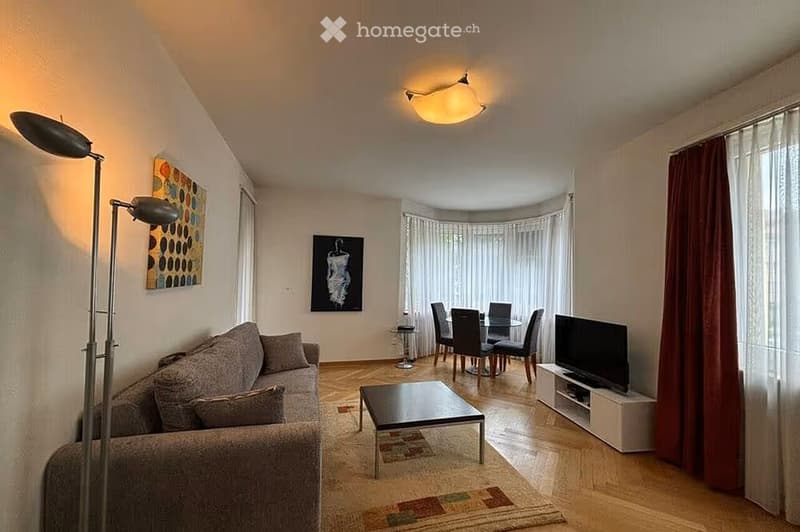 Modern living and dining area with a grey sofa, coffee table, dining table with chairs, TV, floor lamp, and artwork on the walls.