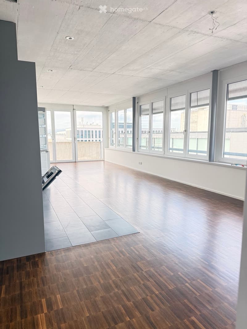 Empty room with wooden flooring, large windows, and a sliding glass door leading to a balcony area.