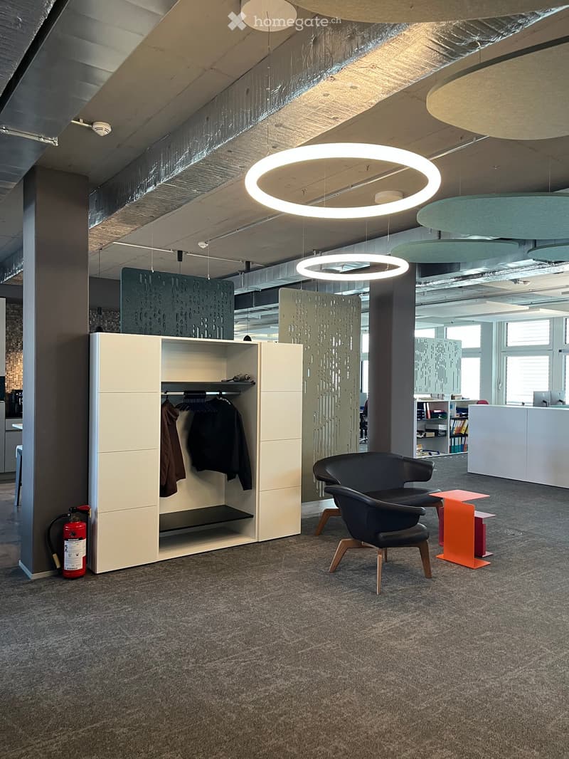 Modern office space with grey carpet, white cabinet, black chairs, orange tables, and circular pendant lights.