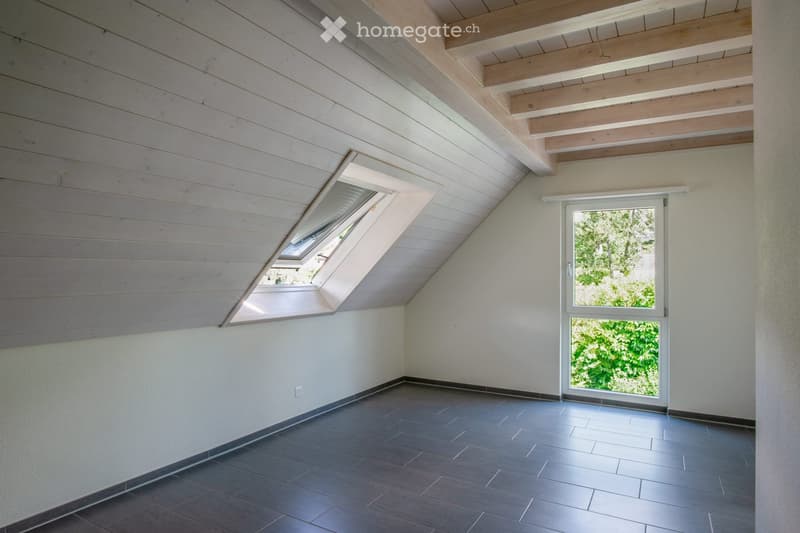 Empty room with wooden ceiling, dark tiled floor, white walls, and large windows including a skylight and a door leading outside.