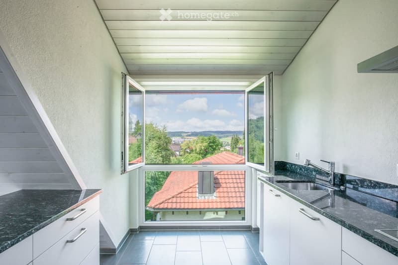 Modern kitchen with white cabinets, granite countertops, and a large window offering a scenic view of the countryside.