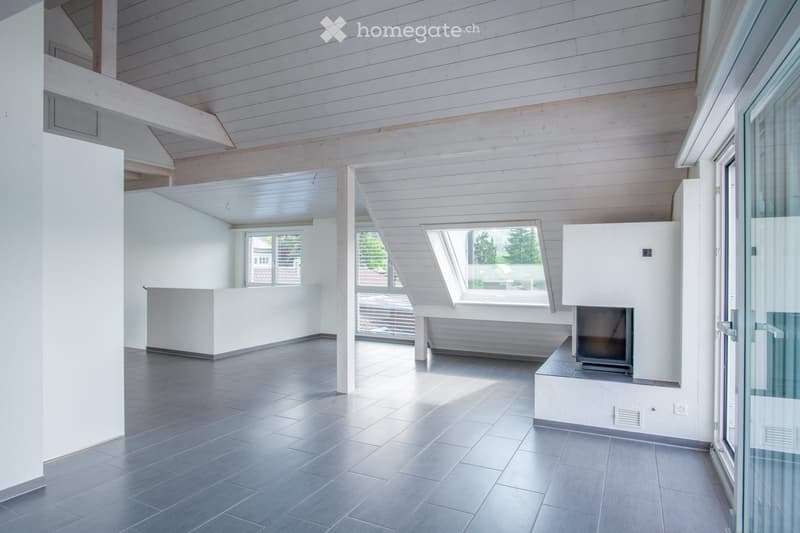 Modern, minimalist room with exposed wooden beams, large windows, and a built-in fireplace. The space is completely empty, with no furniture or decorations.