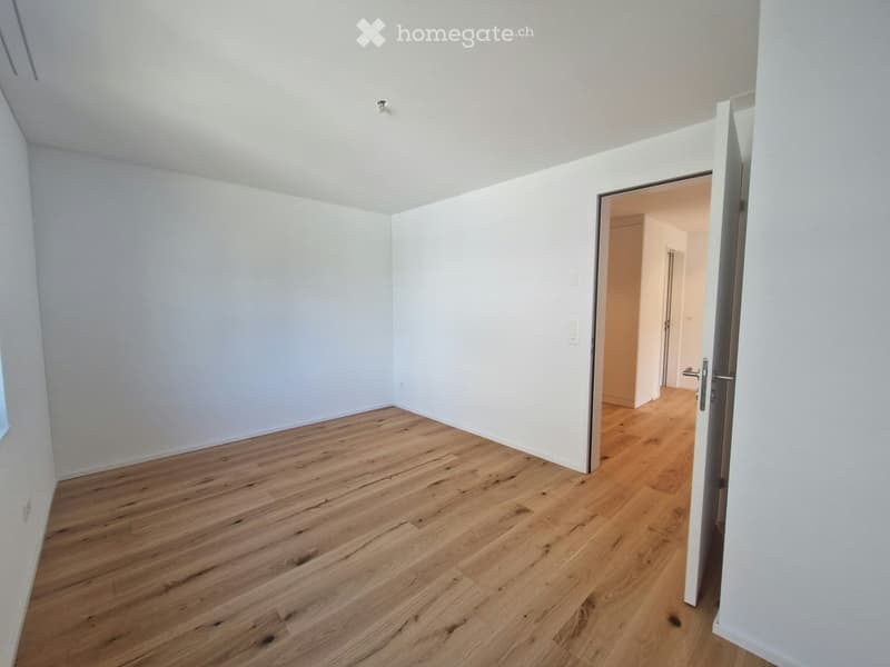 Empty room with light wooden flooring and white walls, featuring an open doorway leading to another room.