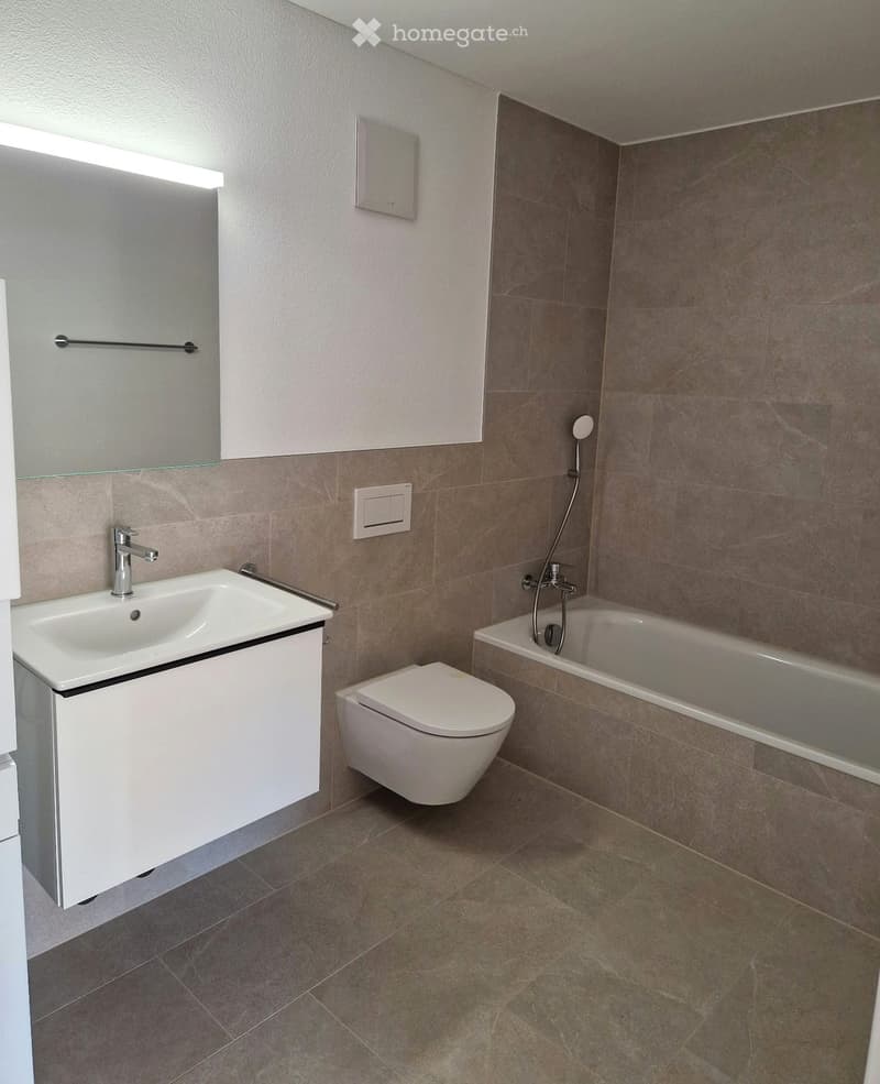 Modern bathroom with a white sink, toilet, bathtub, and showerhead. Features a sleek design with a built-in mirror and modern fixtures.