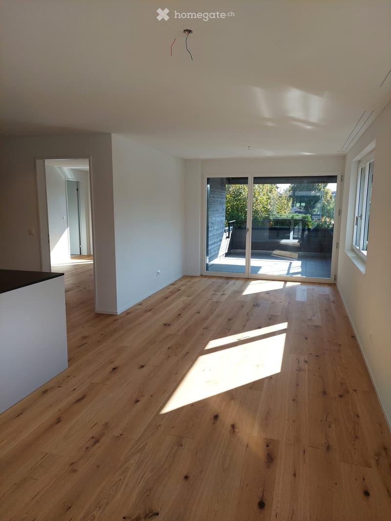 Empty room with light wooden flooring, white walls, and large sliding glass doors leading to a balcony or outdoor area.