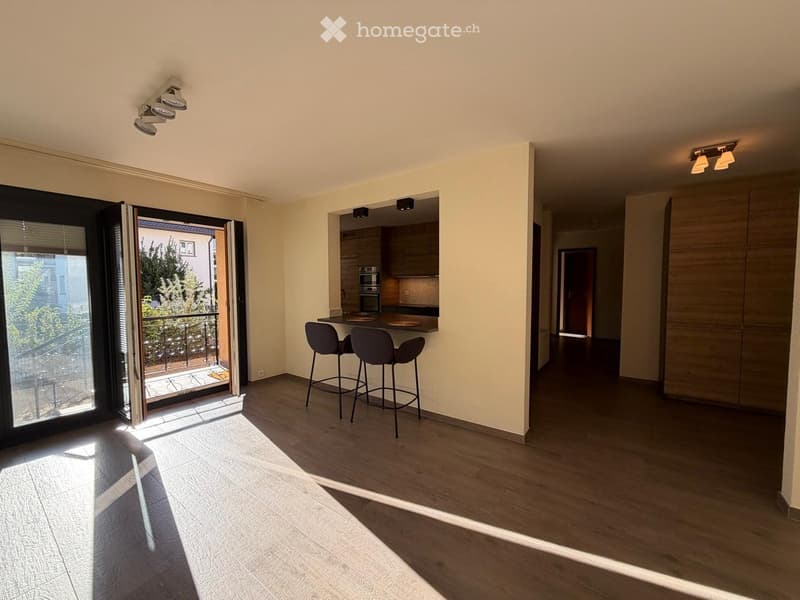 Open-plan living and dining area with wooden flooring, modern kitchen area, and access to a balcony.