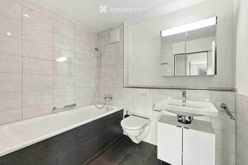 Modern bathroom with a bathtub, toilet, double sink, large mirror, and sleek fixtures.