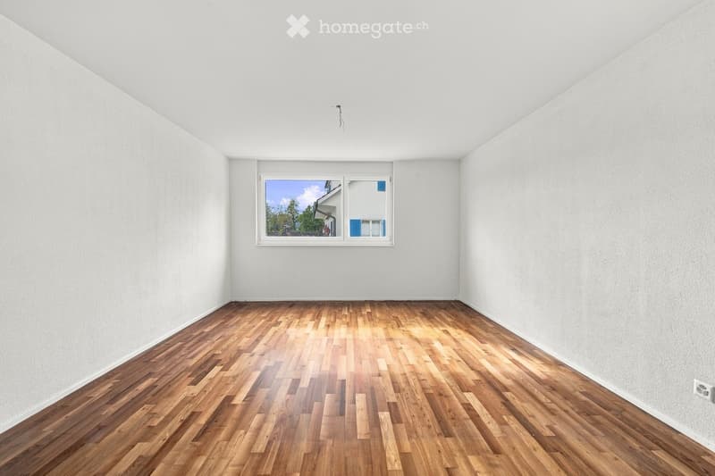Empty room with wooden flooring and white walls, featuring a single window with a view of the outside.