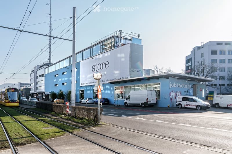 Modern commercial building with a light blue facade, large windows, and signage reading "the store" and "jobfactorys".