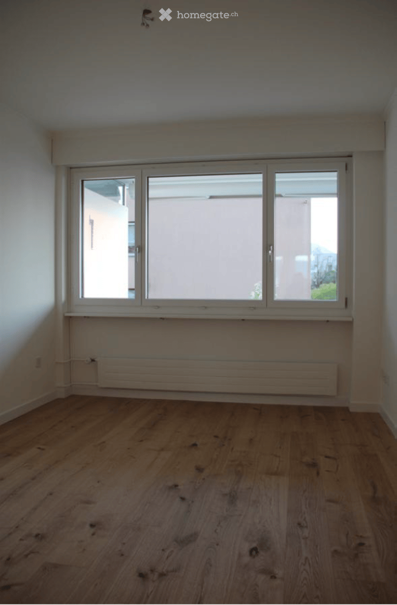 Empty room with wooden flooring, white walls, and large windows with white frames. No furniture or equipment present.