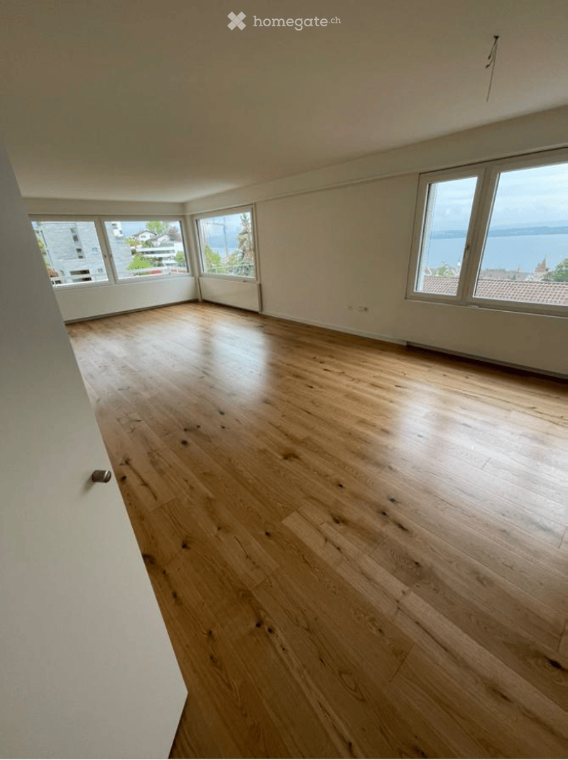 Empty room with wooden flooring and large windows offering a scenic view of the water and surrounding area.