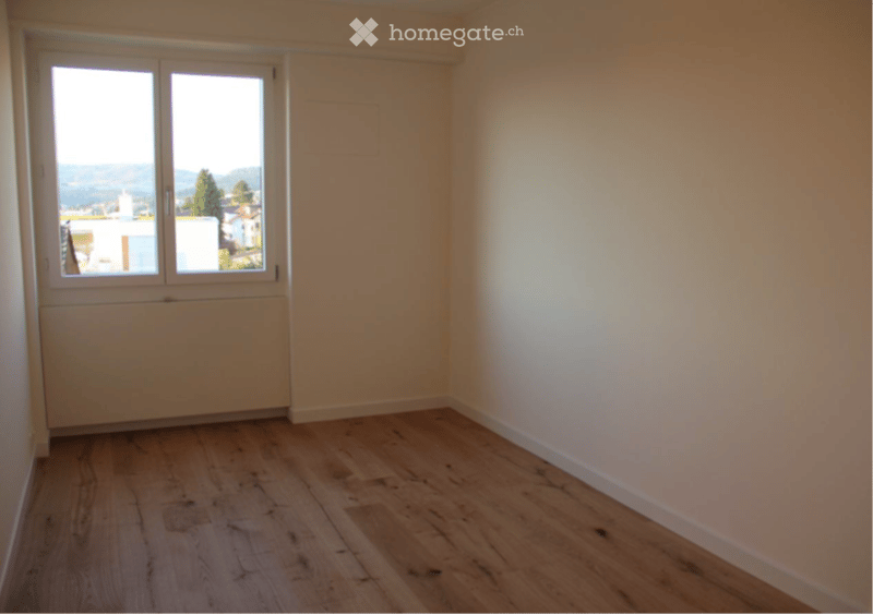 Empty room with wooden flooring, white walls, and large windows offering a scenic view of the landscape.