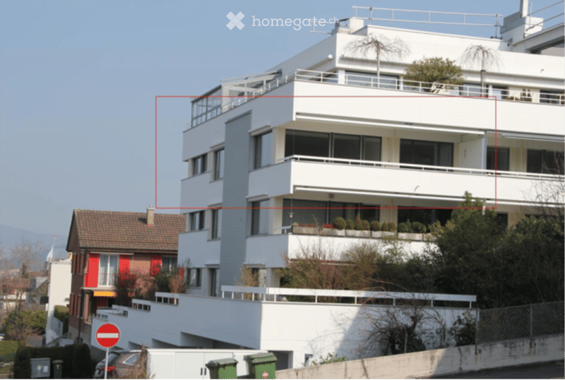 Modern multi-story apartment building with white facade, large windows, and balconies. The building features contemporary design with clean lines and a flat roof.