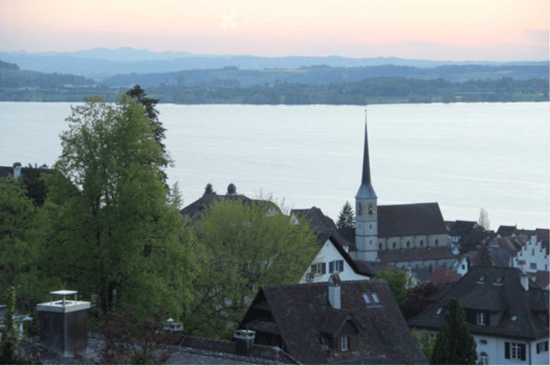 Scenic view of a town with traditional houses, a church tower, and a lake in the background during sunset.