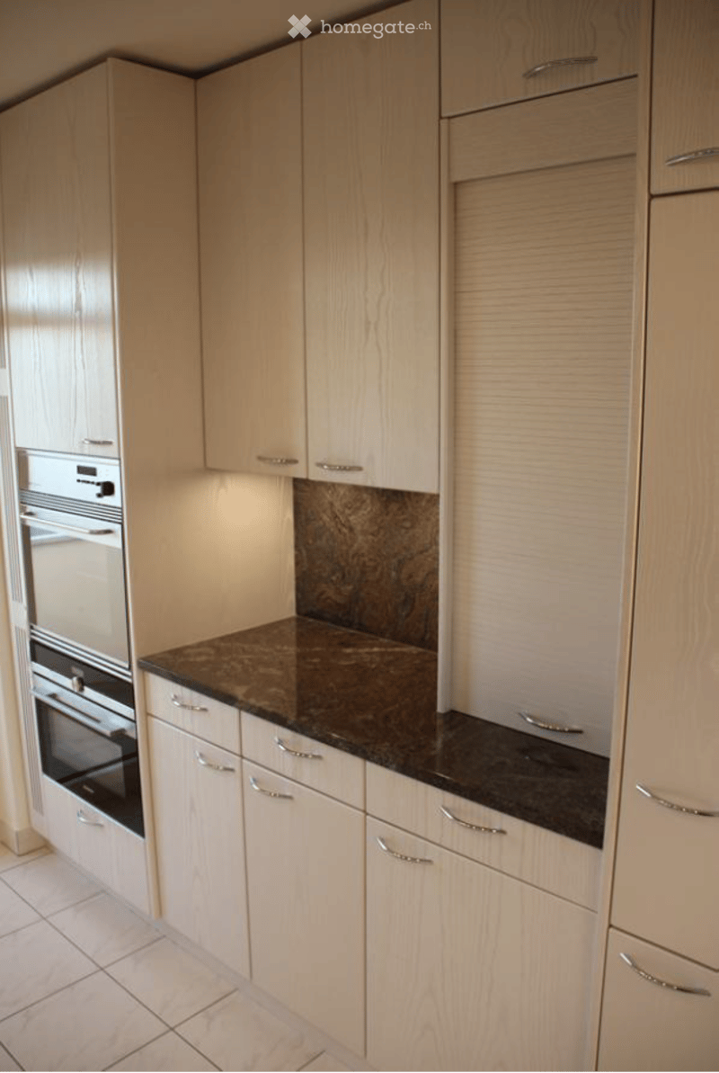 Modern kitchen with light wood cabinets, stainless steel oven, and dark granite countertop.
