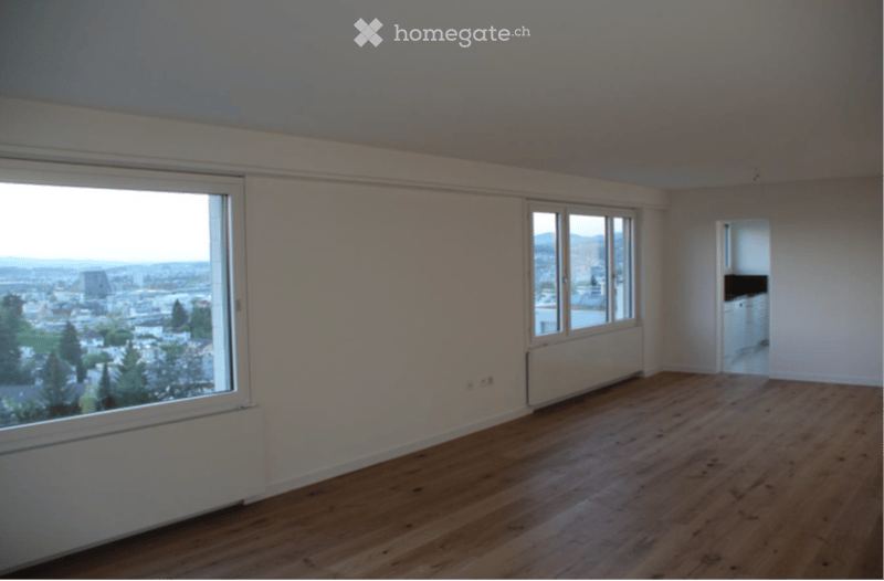 Empty room with wooden flooring, large windows offering a city view, and a radiator under one window.