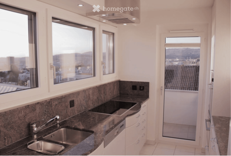 Modern kitchen with stainless steel sink, granite countertop, white cabinets, and large windows offering a city view.