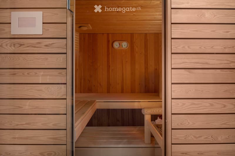 Modern sauna with wooden benches, glass door, and control panel on the wall.