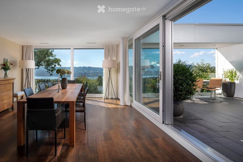 Modern dining room with wooden floor, large windows, scenic view, dining table with chairs, floor lamps, vase, candle, and cabinet.