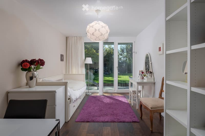 Modern bedroom with a bed, purple rug, white shelves, a small table with a mirror, and a vase with flowers on a nightstand.