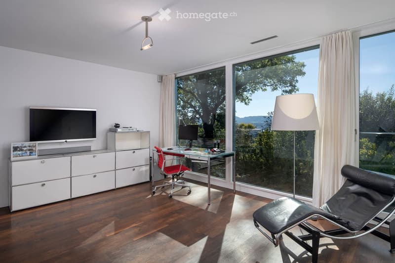 Modern room with large windows, wooden floor, a red chair, a glass table, a screen, a cabinet, and a lamp.