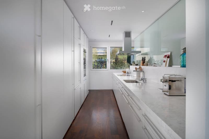 Modern kitchen with white cabinets, marble countertops, and a stainless steel sink. Features a coffee maker and various kitchen utensils on the counter.