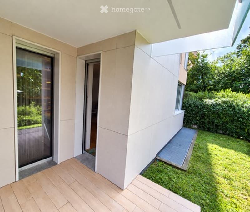 Modern balcony with wooden decking, large glass sliding door, and a view of a green garden area.