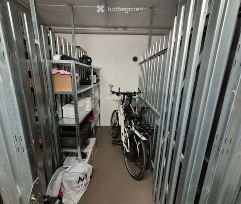 Empty storage room with metal shelving units, bicycles, and some boxes and bags on the floor.