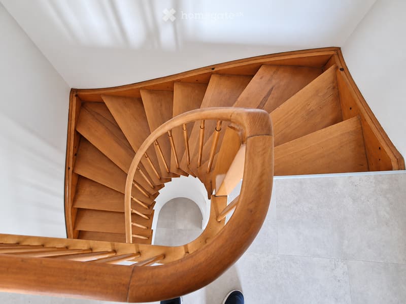 Spiral wooden staircase with a curved handrail and open design, leading upwards.
