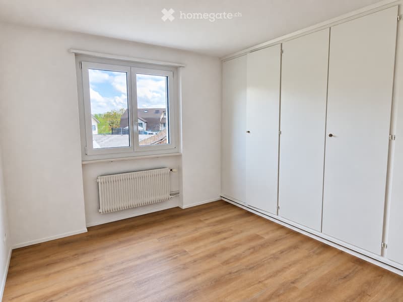 Empty room with light wooden flooring, white walls, built-in white closet, and a window with a view of the outside.