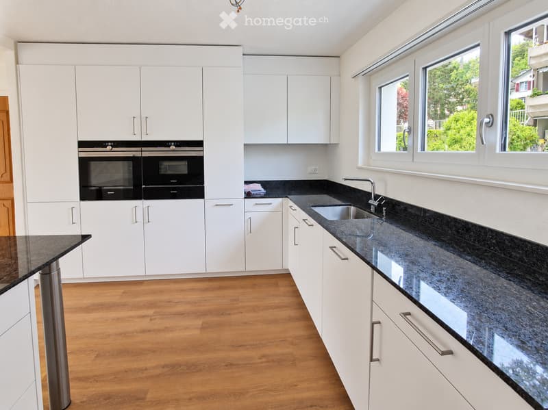 Modern kitchen with white cabinets, black granite countertops, stainless steel sink, and built-in ovens.
