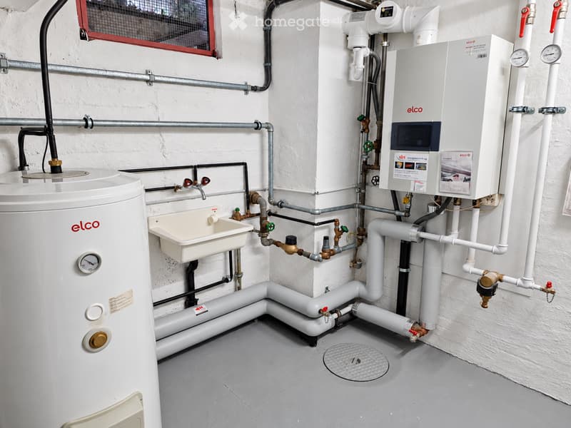 Utility room with a water heater, sink, and various pipes and valves.