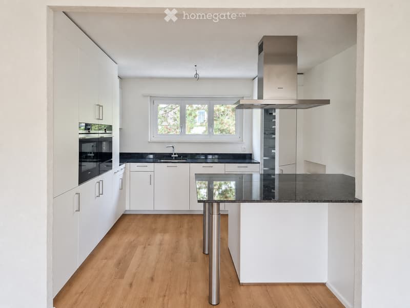 Modern kitchen with white cabinets, stainless steel appliances, a central island with a glass top, and a wooden floor.