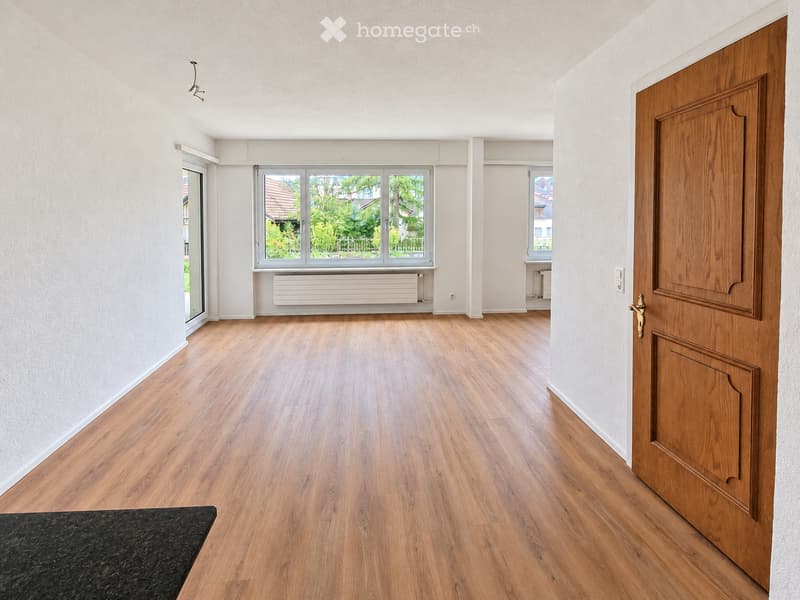 Empty room with wooden flooring, white walls, large windows, and a radiator. No furniture or equipment present.