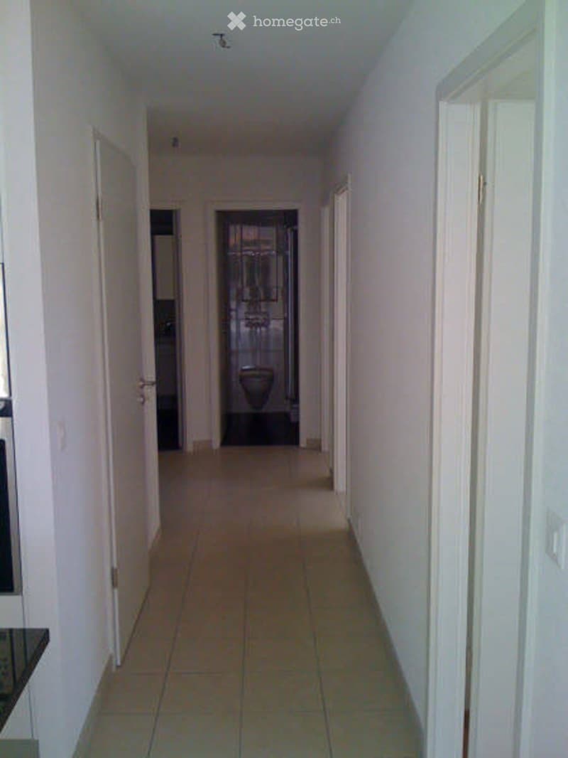 Empty hallway with tiled floor, white walls, and several doors leading to rooms.