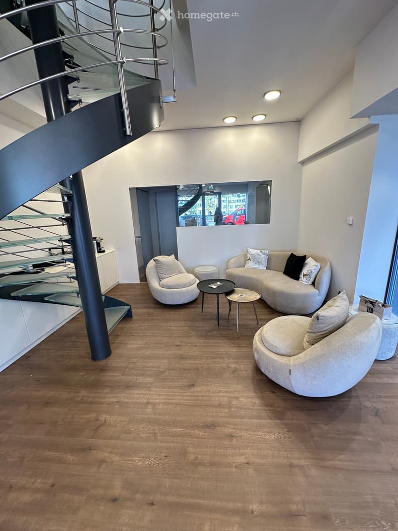 Modern living room with wooden flooring, white walls, and contemporary furniture including a curved sofa, armchairs, and small tables.