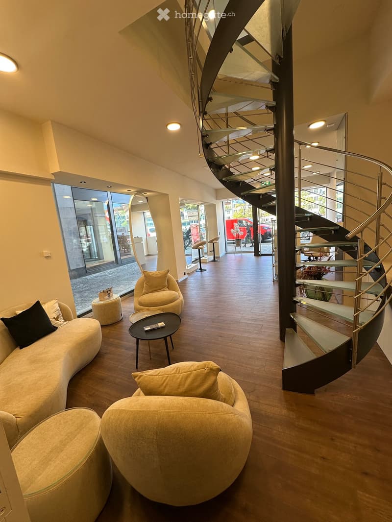 Modern living room with a curved sofa, coffee table, chairs, and a staircase leading to another level.