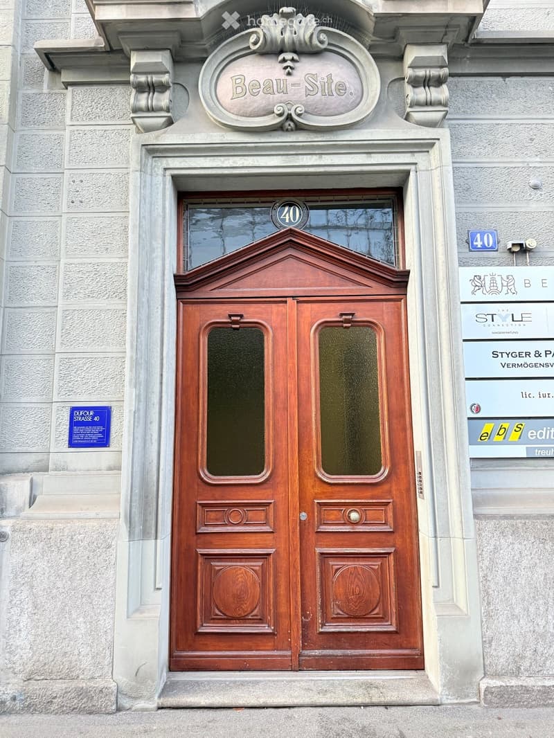Ornate wooden double doors with glass panels, decorative stone surround, and signage above reading "Beau-Site."