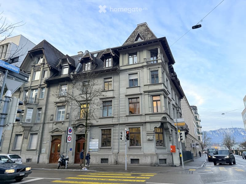 A multi-story building with classic architecture, large windows, and ornate details, located on a street corner with traffic signs and vehicles nearby.