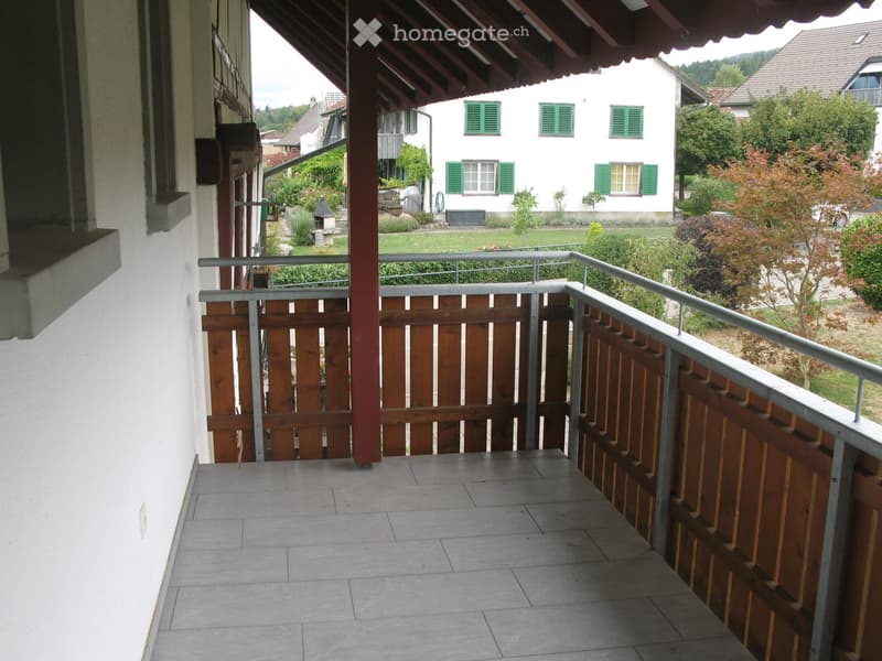 Balcony with tiled floor, wooden railing, and metal balustrade, overlooking a garden and neighboring house.