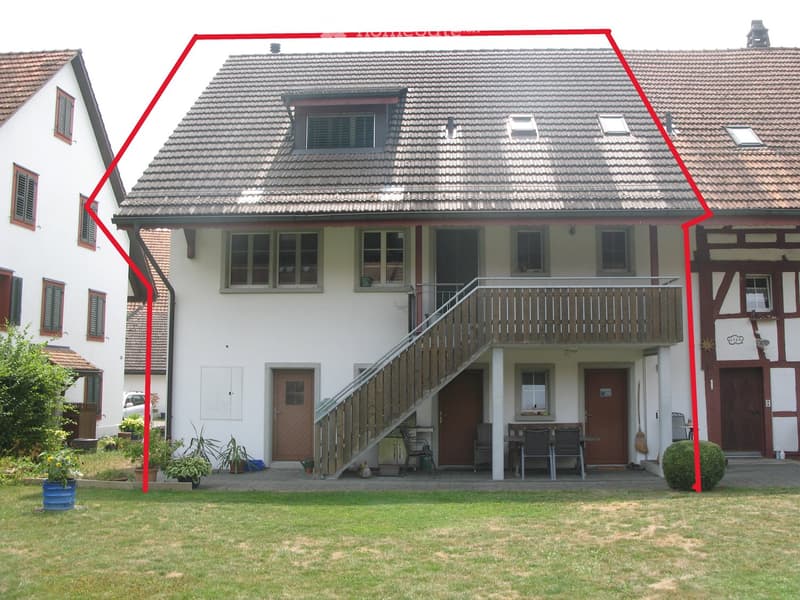 Two-story house with a tiled roof, white exterior, multiple windows, and a covered balcony area with outdoor furniture.