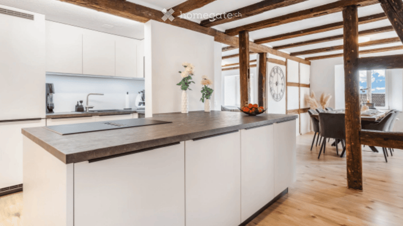 Modern kitchen with white cabinets, wooden beams, island, sink, and dining area with chairs and table.