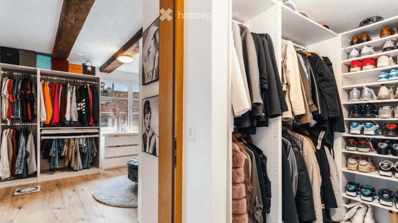 Spacious walk-in closet with built-in wardrobes, shelves, and drawers. Features a large mirror, a small stool, and a round rug in the adjacent room.