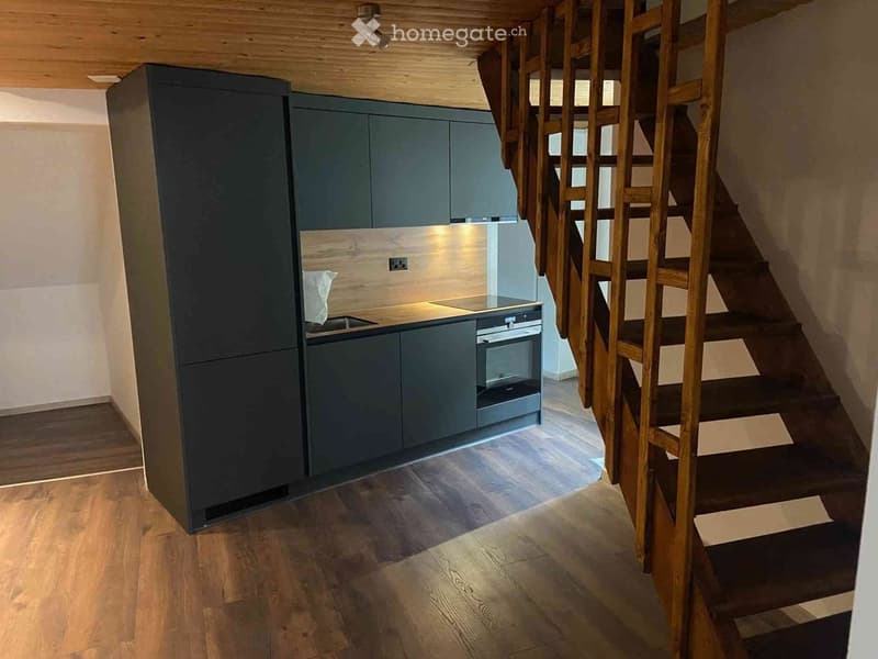 Modern kitchen with grey cabinets, stainless steel appliances, and a wooden staircase leading to an upper level.