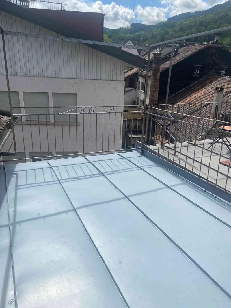 Roof terrace with metal railing, clear plastic cover, and a small table and chairs in the corner.