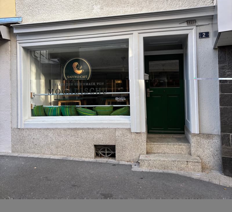Facade of a small cafe with a green door, large window displaying cushions, and signage for 'SafiYo Cafe' and 'Mogadischu'.