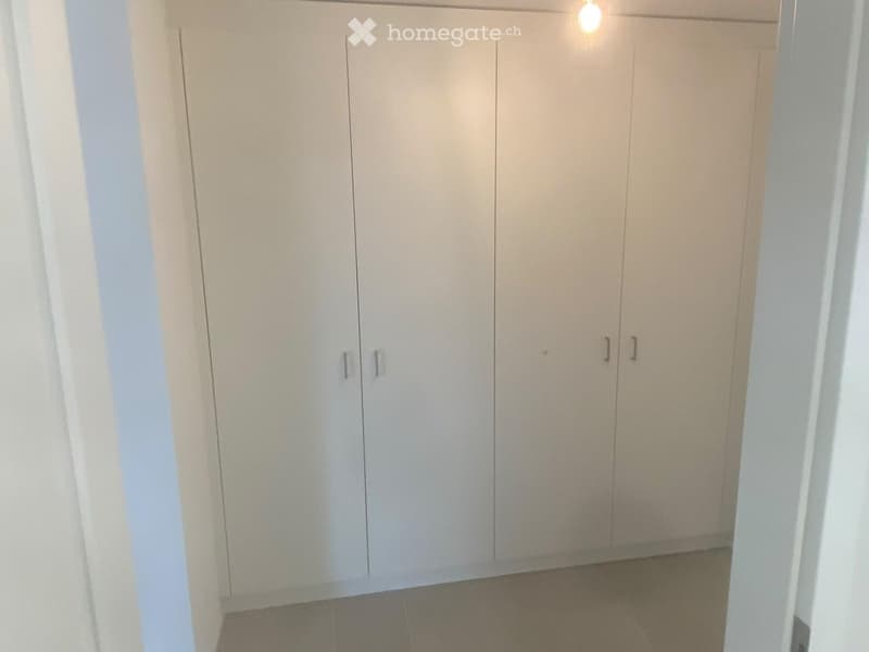Empty room with white built-in wardrobes and tiled floor.
