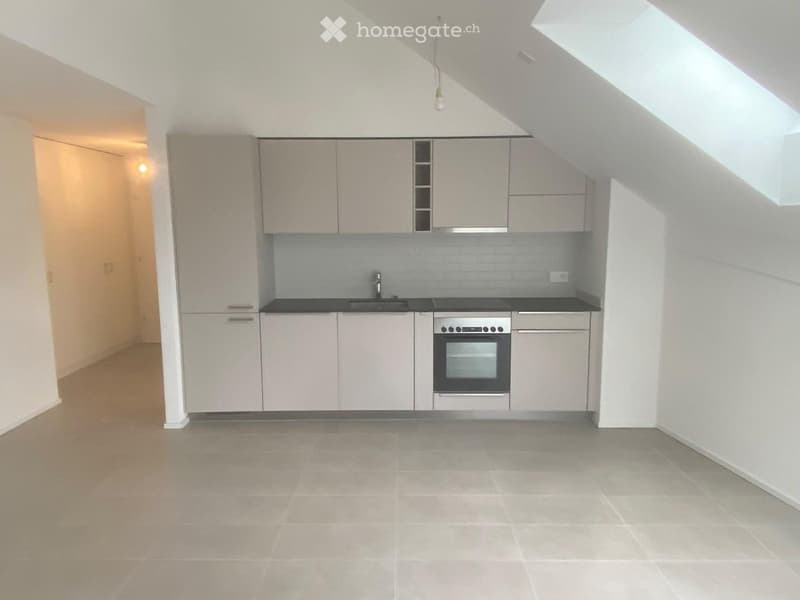 Modern, minimalist kitchen with light grey cabinets, a black countertop, and built-in appliances including a sink and oven. The space features tiled flooring and ample natural light from a skylight.